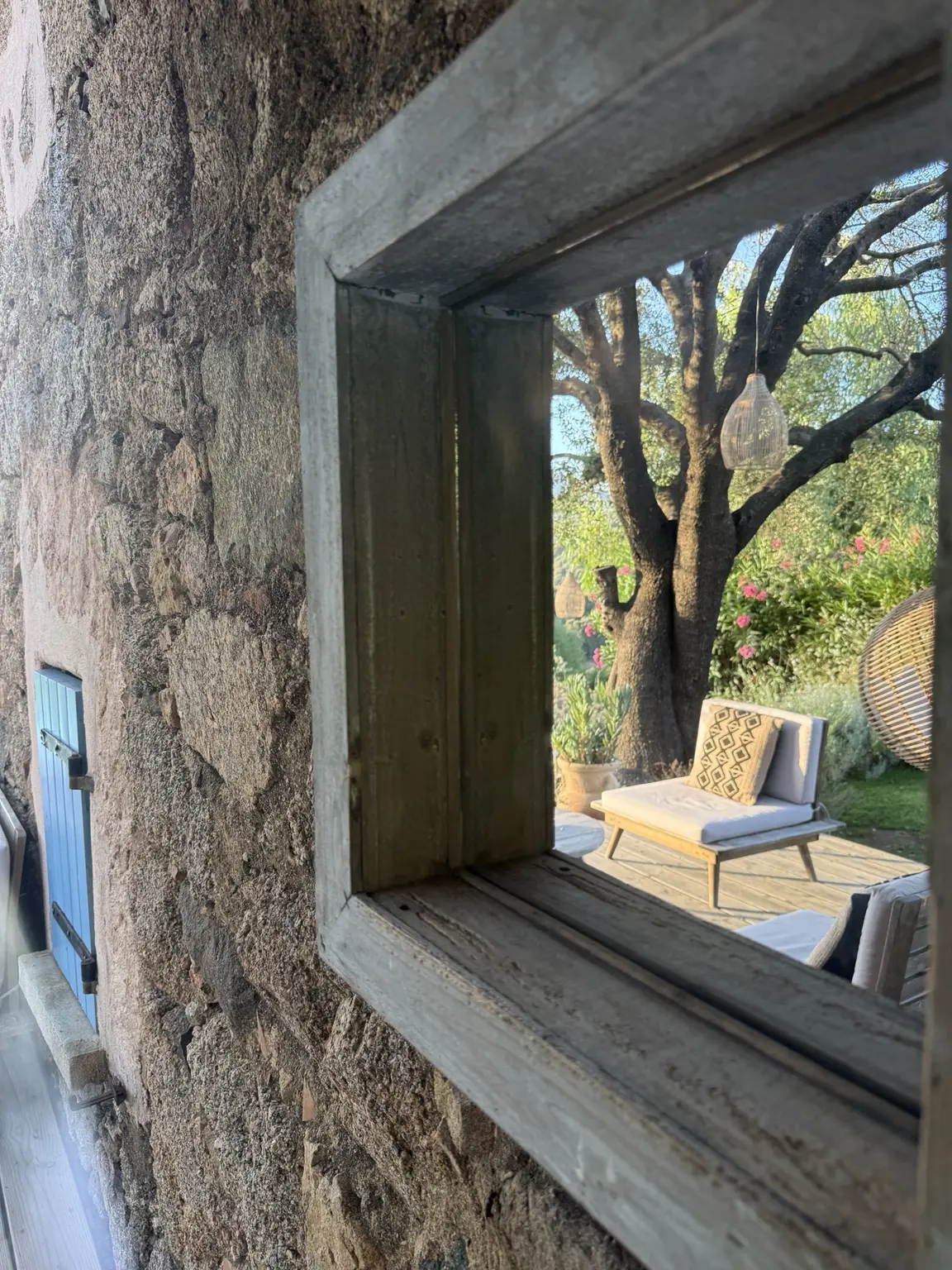 Reflet de l’olivier et de la terrasse dans un miroir sur le mur en pierre